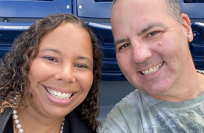 Darnetta and John Yusko sitting in front of a blue stadium seating background.
