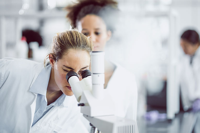 Two doctors. One is looking into a microscope.