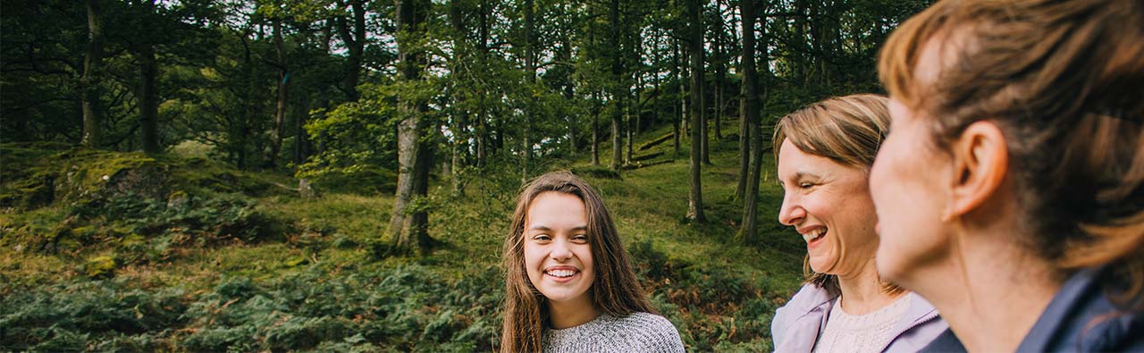 Teenage girl and her little borther are talking to their mother and grandmother as they hike through the woodlands together.