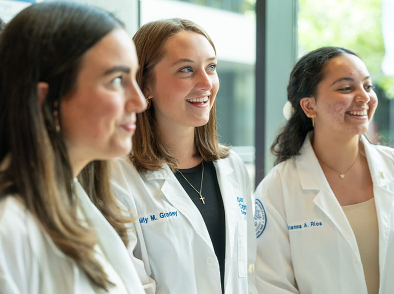 Three female students stand outside smiling