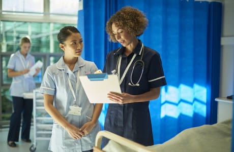 A senior nurse talks with a new nurse holding a clipboard