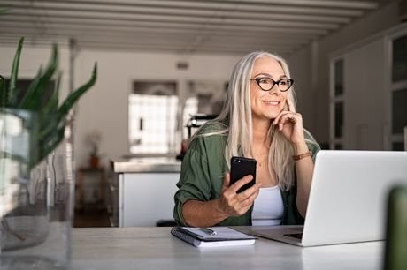 Senior woman using a laptop and smartphone in her home
