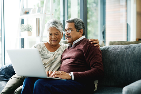 Older couple sitting on a couch, researching on a laptop.