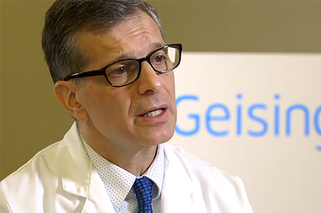 A man wearing glasses and a white lab coat speaks, with a partially visible "Geisinger" sign in the background.