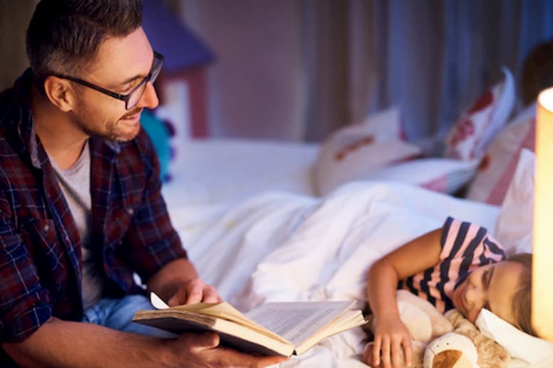Man reading girl book at bedtime.