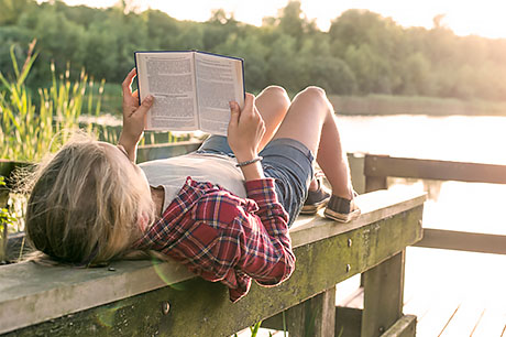 Young male student reading on a dock at sunrise.
