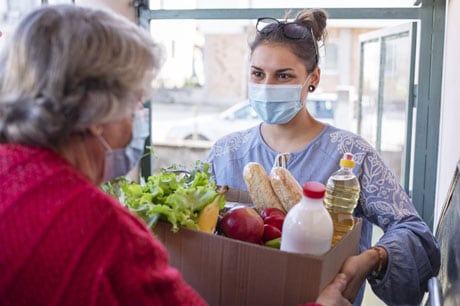 young woman wearing mask delivering groceries to an elderly woman