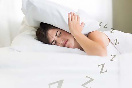 A woman covers her head with a pillow as she struggles to get some sleep.