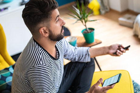 Man sitting on a couch, holding a smartphone and TV remote.
