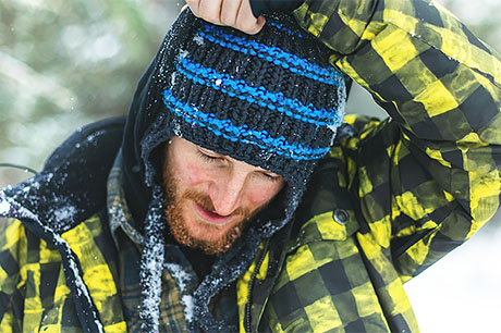 A young man in the snow pulls up his hood to get additional protection from the cold.