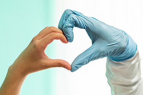 A young patient and provider make a heart shape with their hands.