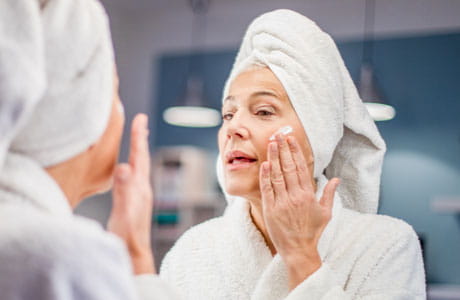 Woman rubbing lotion on her face. 