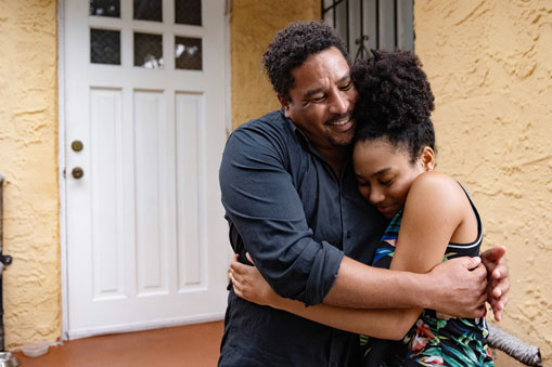 Father hugging teen daughter in front of their house