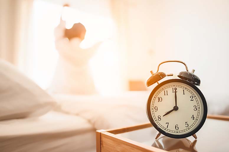 A woman wakes to a sunrise through her bedroom windows.